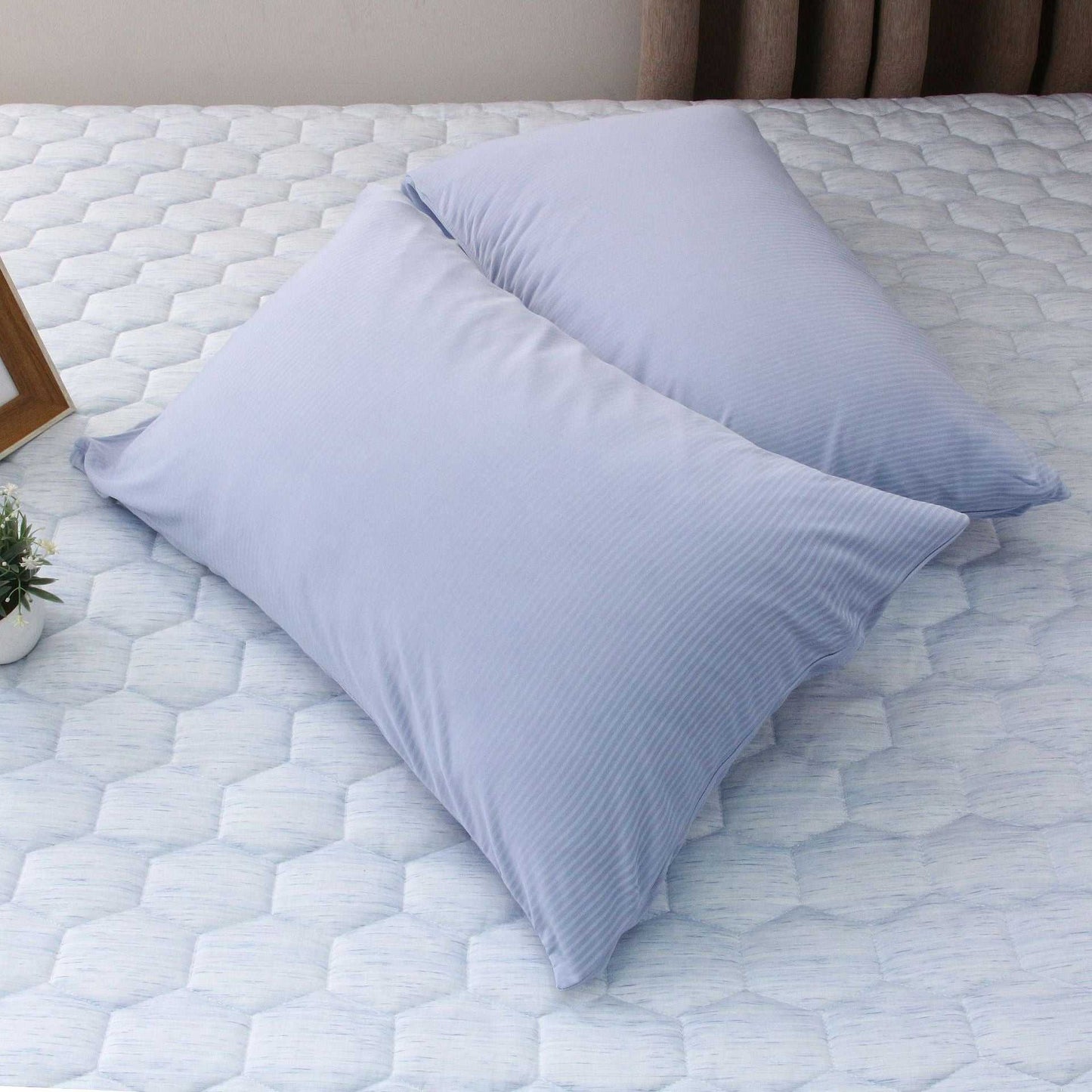 Light blue summer cooling blanket and pillow on a mattress.