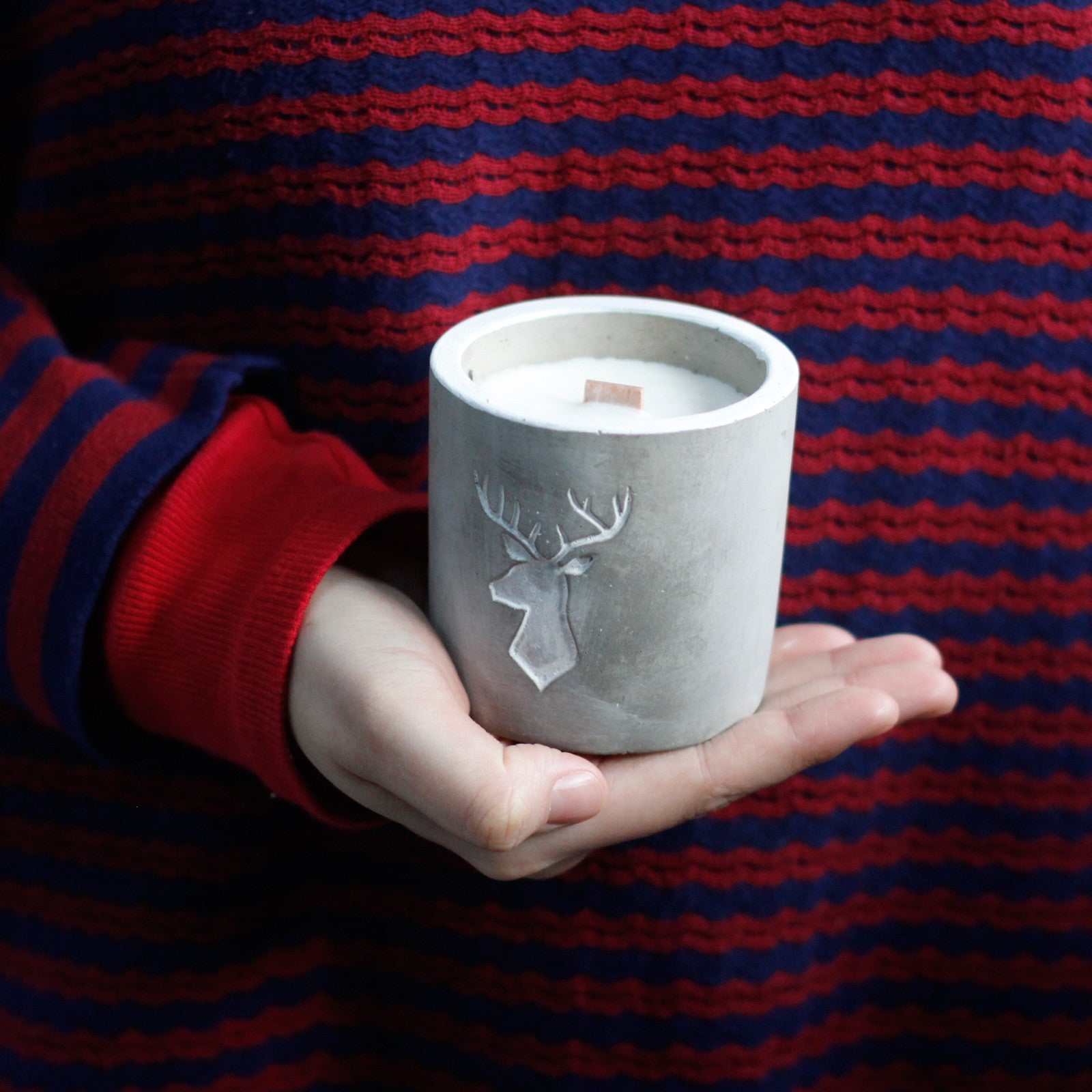 Medium concrete pot candle with wooden wick, featuring raw finish, held in hands.