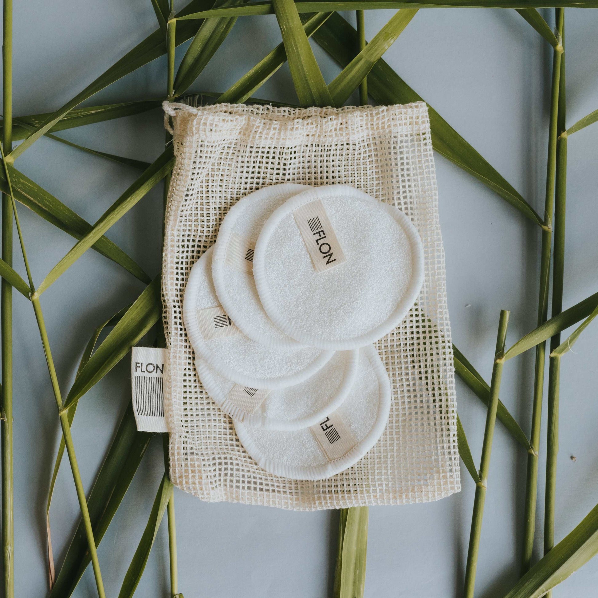 Reusable bamboo makeup remover pads with mesh storage bag on green bamboo background.